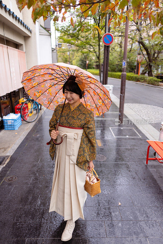 穿着和服/袴的年轻女子在下雨天走在城里